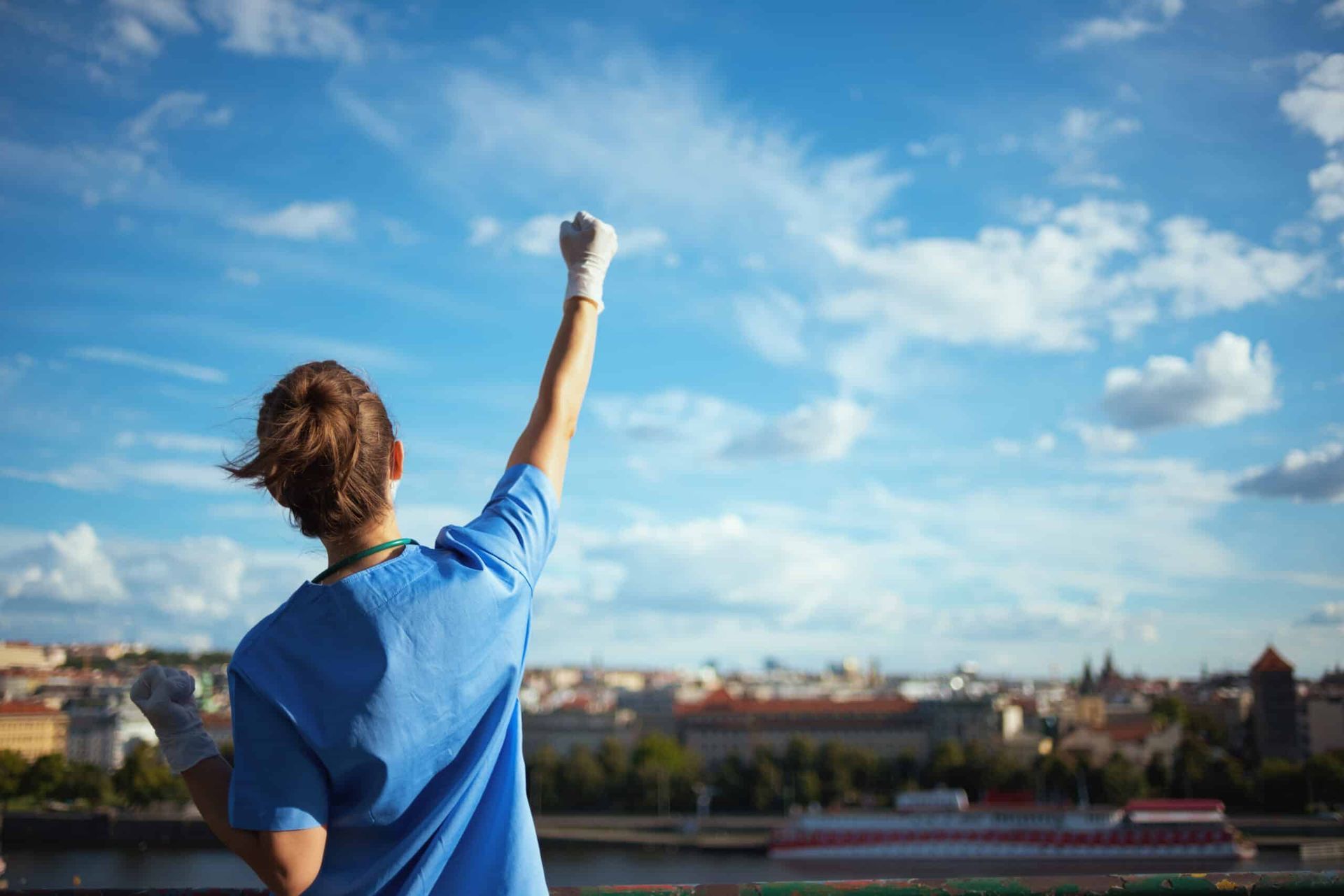 Nurse with raised fist against blue sky overlooking cityscape.