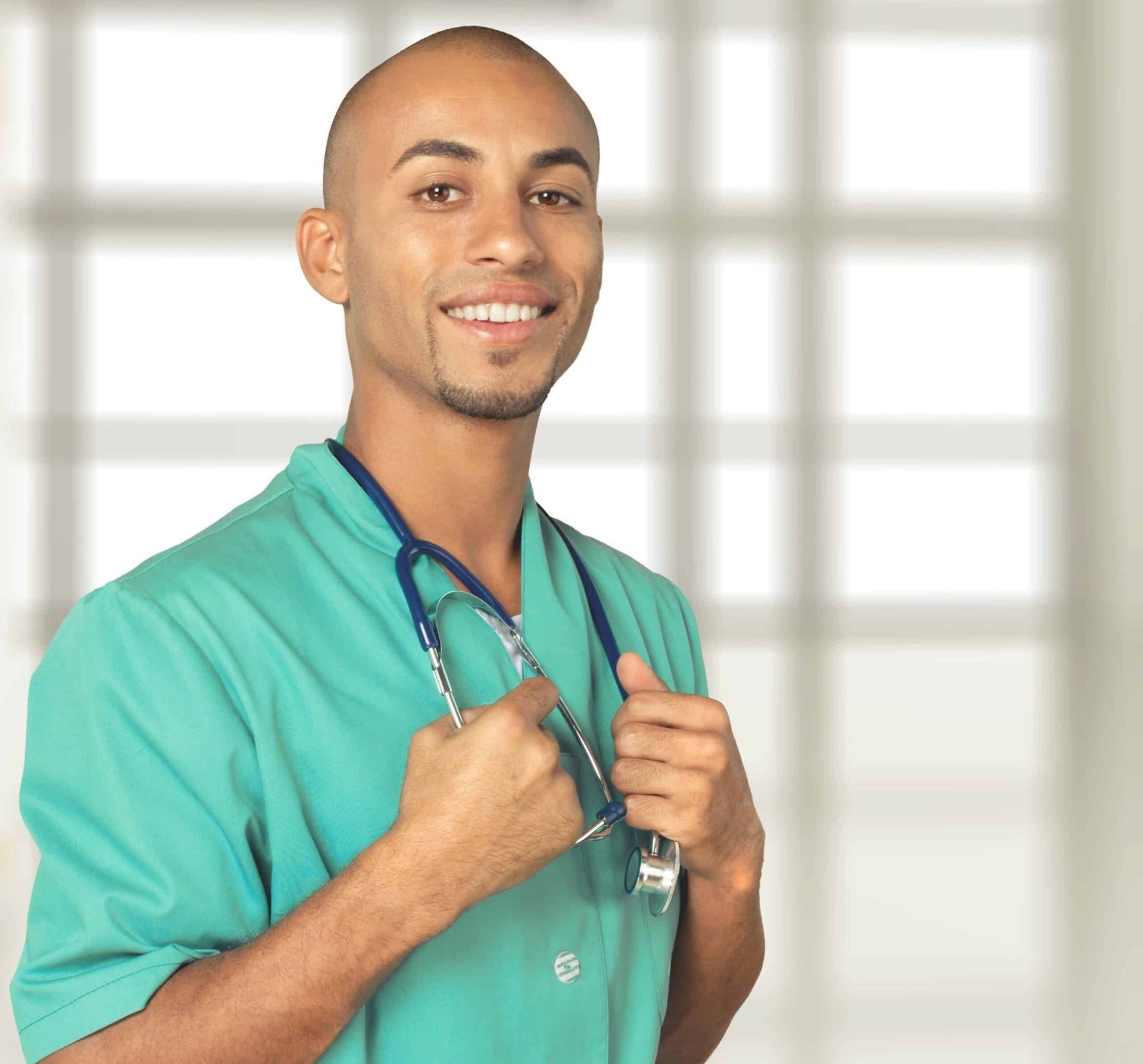 Smiling male doctor with stethoscope, wearing green scrubs, standing in a medical setting.