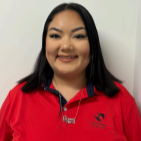 Smiling person in a red collared shirt standing against a plain light-colored wall