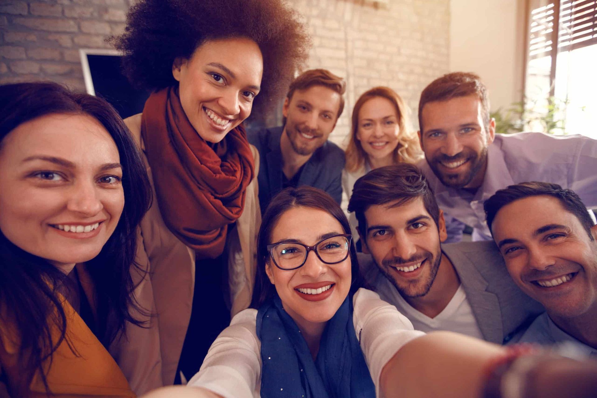 Group of diverse people smiling and taking a selfie indoors.