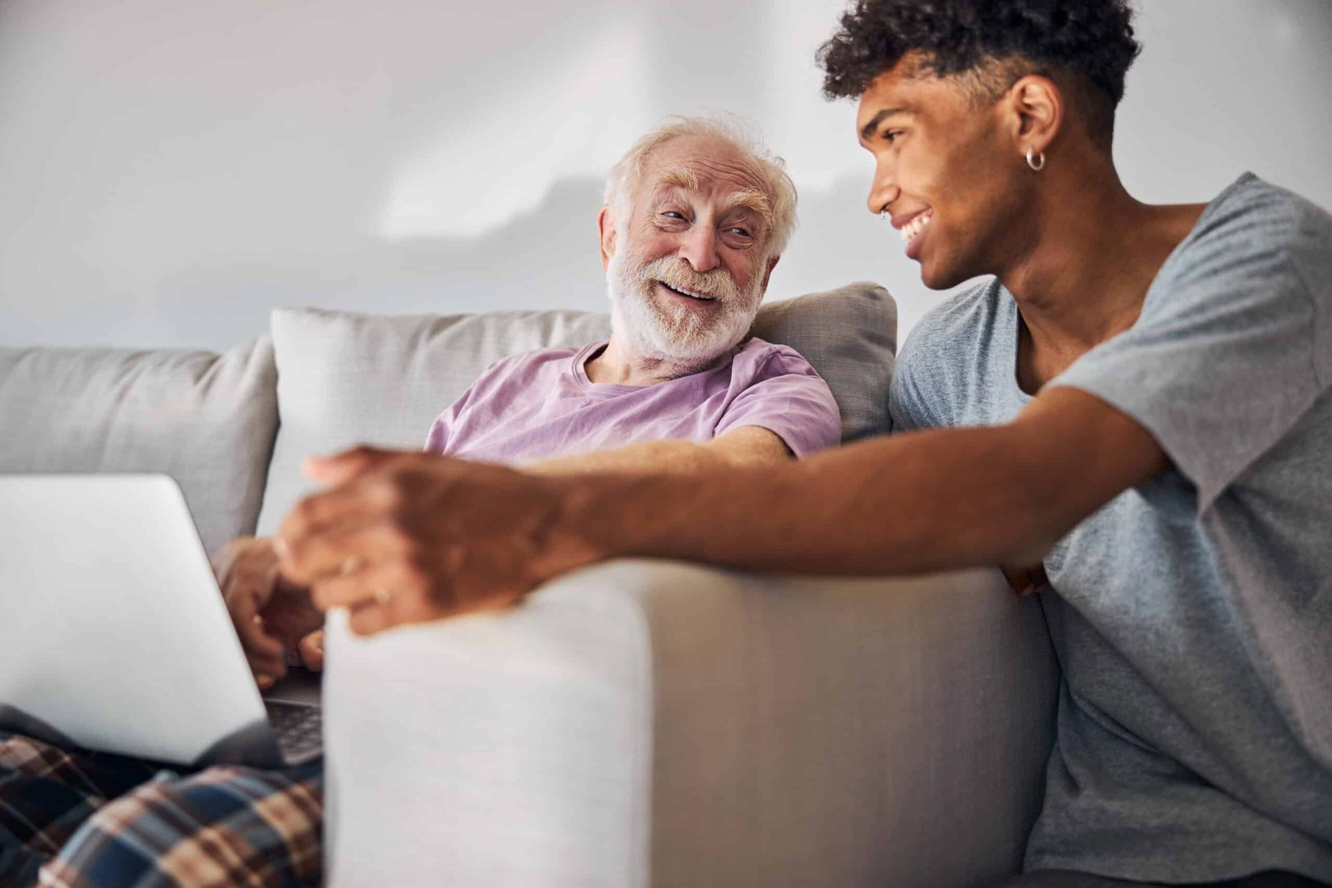 Two people sitting on a couch, smiling and using a laptop together