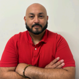 Man in a red polo shirt with folded arms, posing against a plain light background.