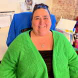 Smiling person in a bright green cardigan seated at a desk in an office setting