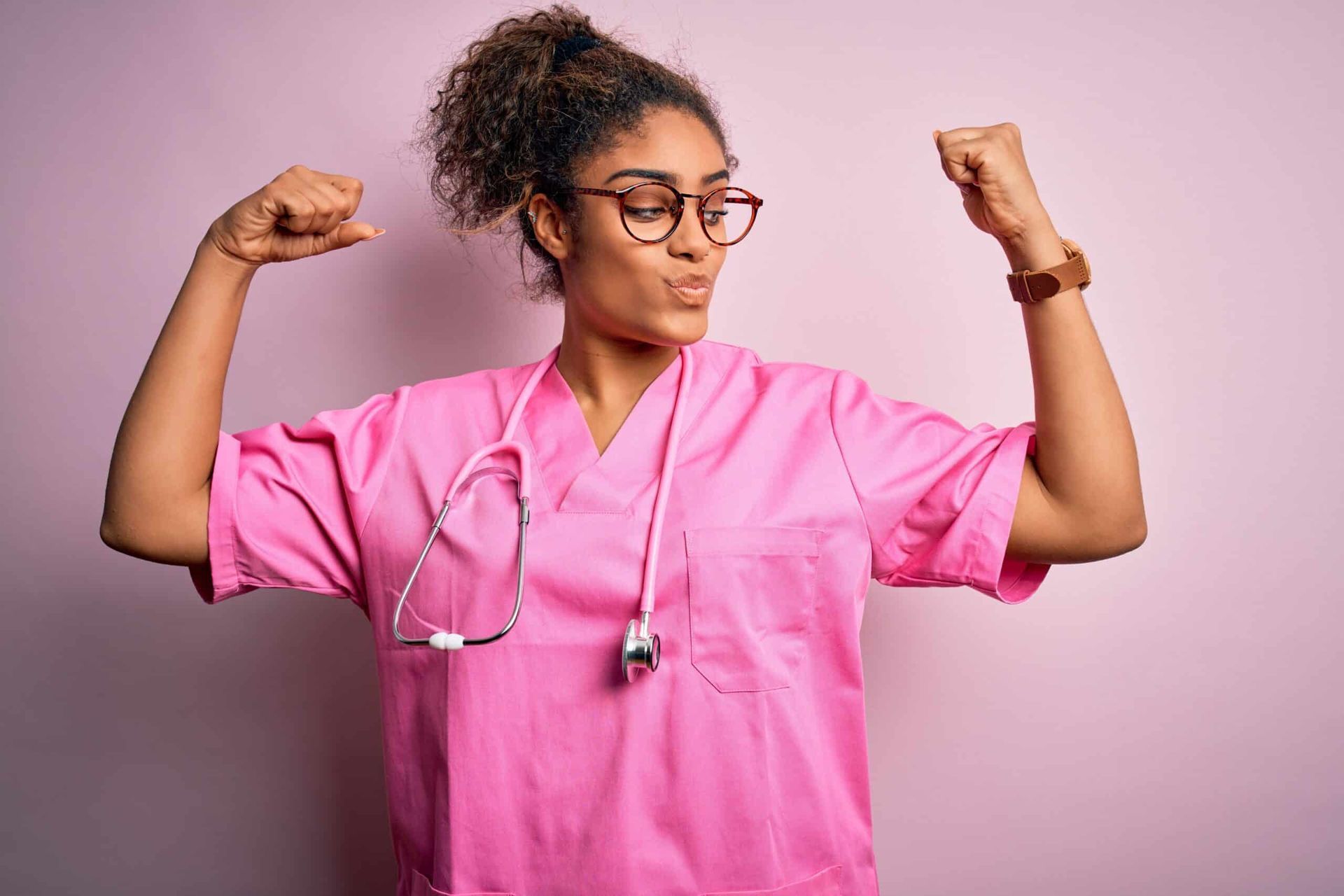 Nurse in pink scrubs flexing her arms, looking strong.