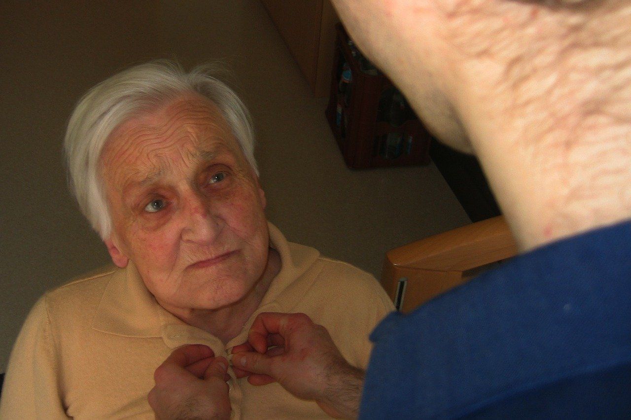 An elderly woman has her shirt buttoned by someone out of view.