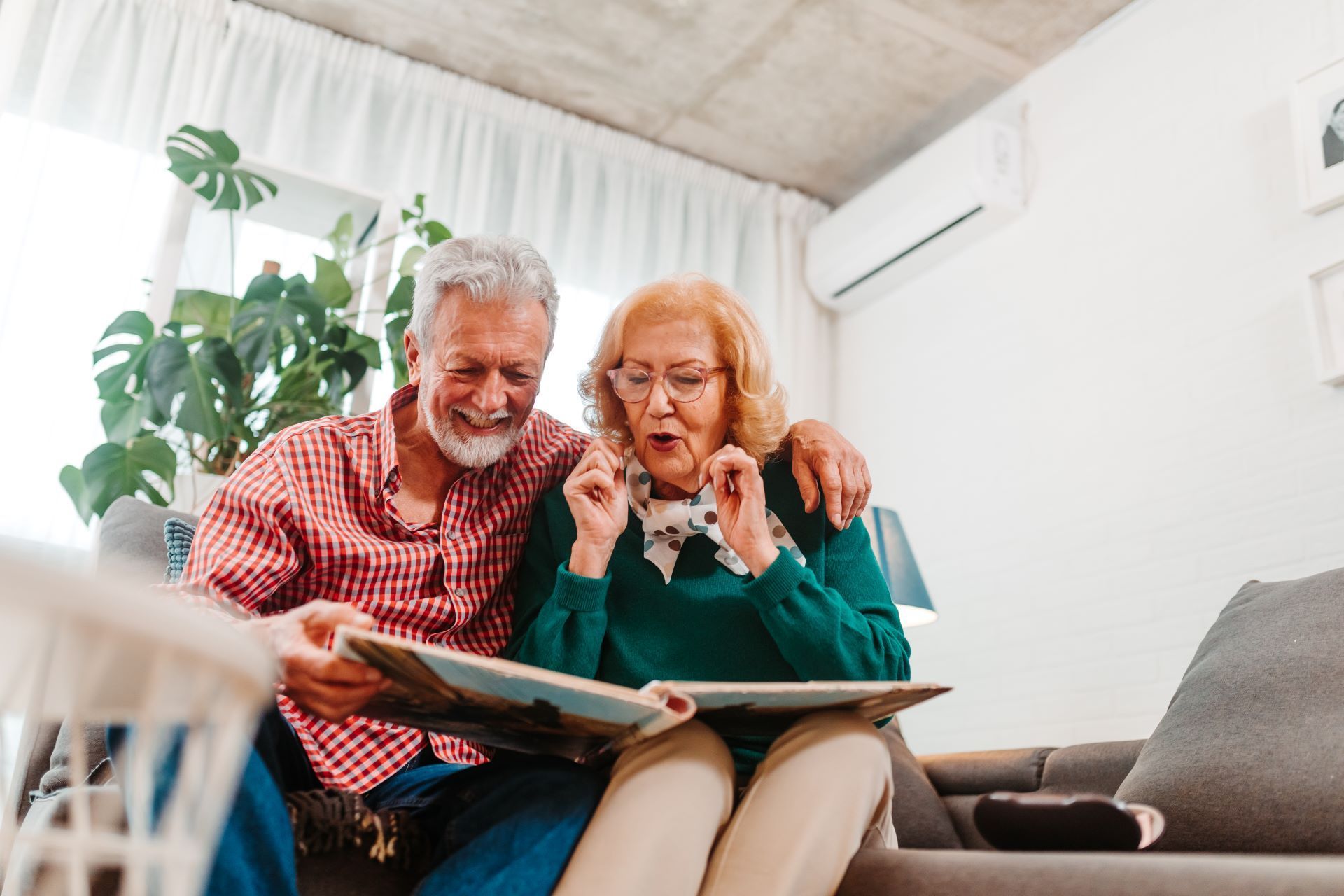 Two people on a couch reading a book together in a bright living room