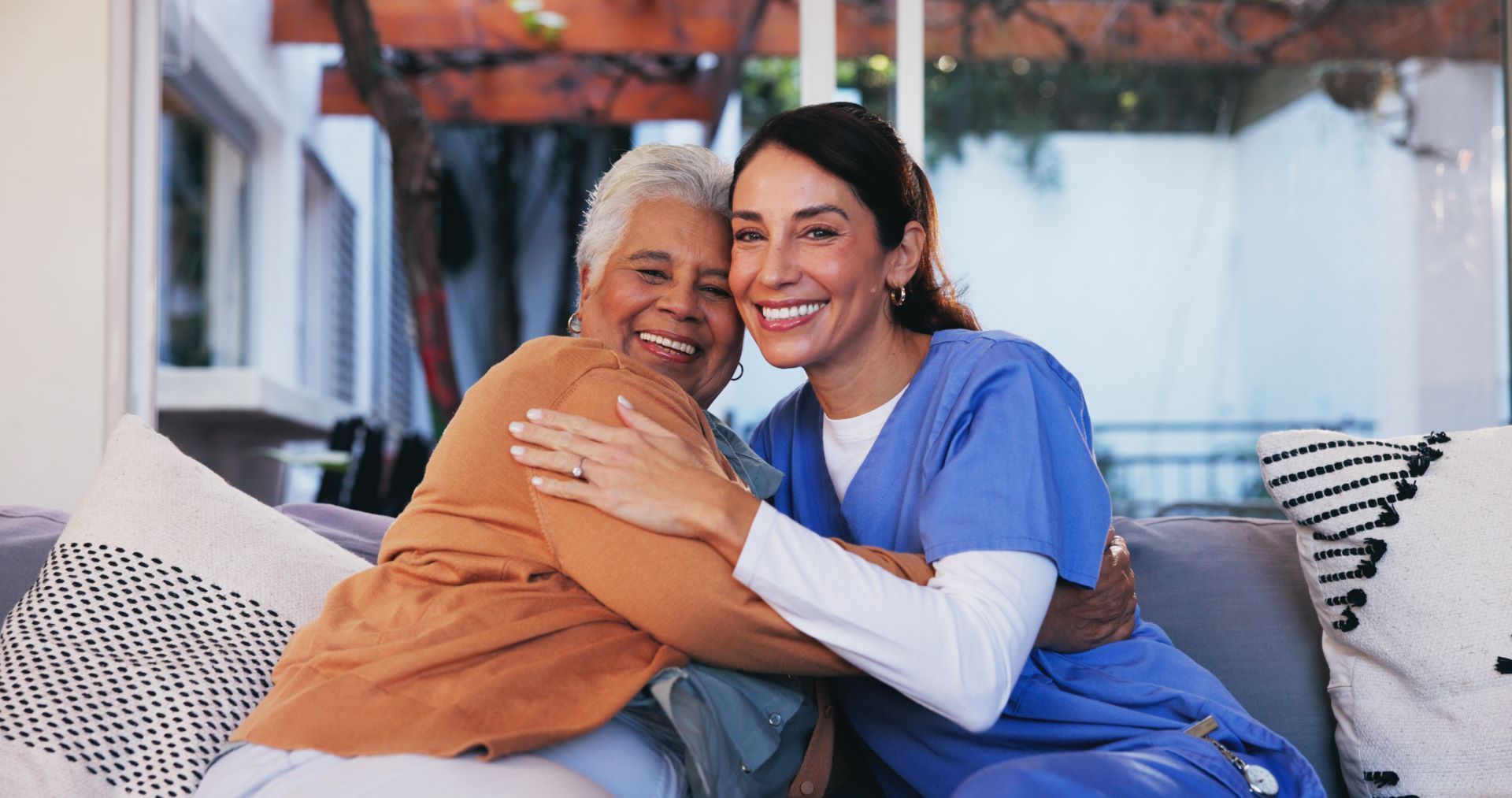Two people smiling and hugging on a couch in a bright living room