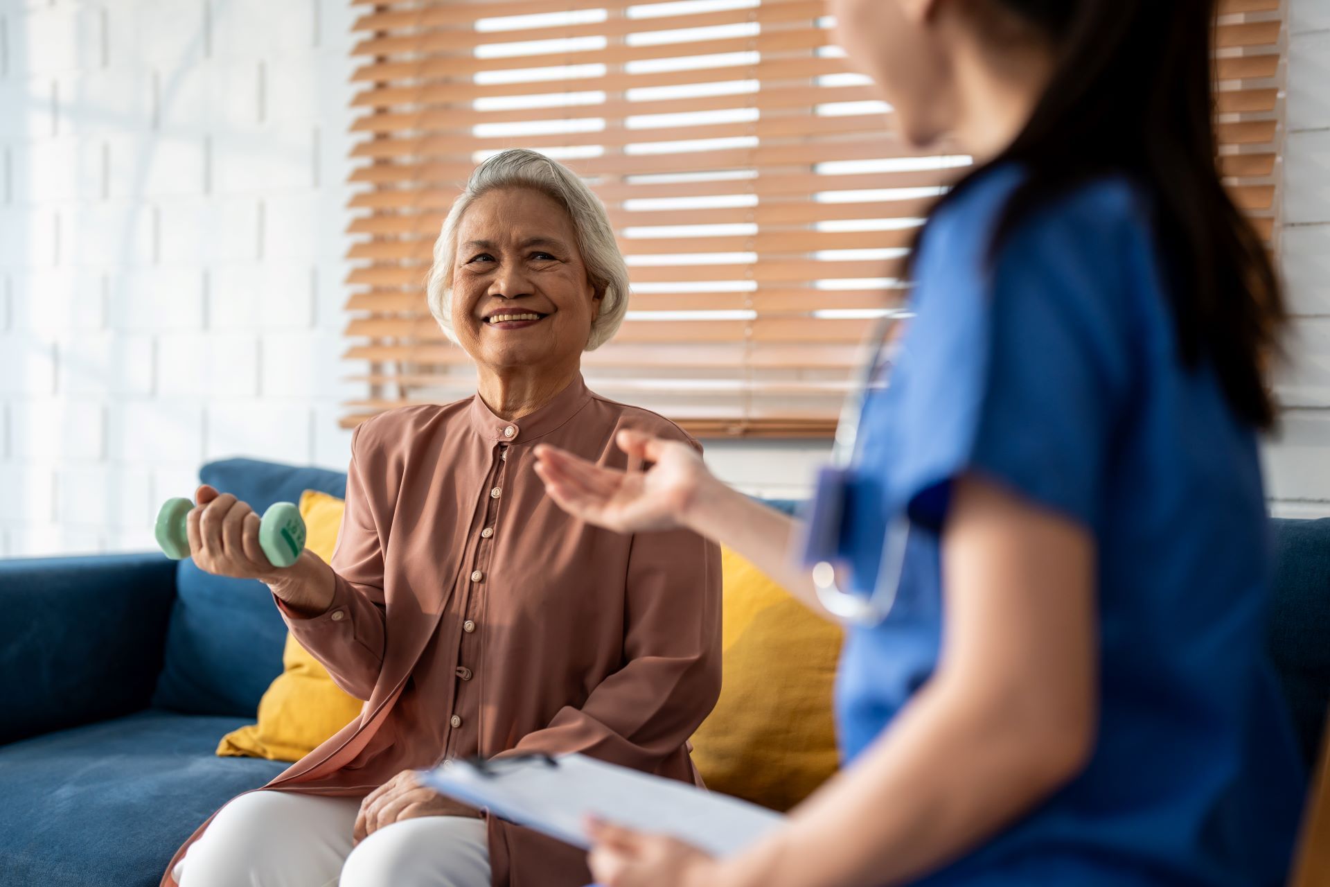 Woman holding a dumbbell while talking with a clinician in a bright living room