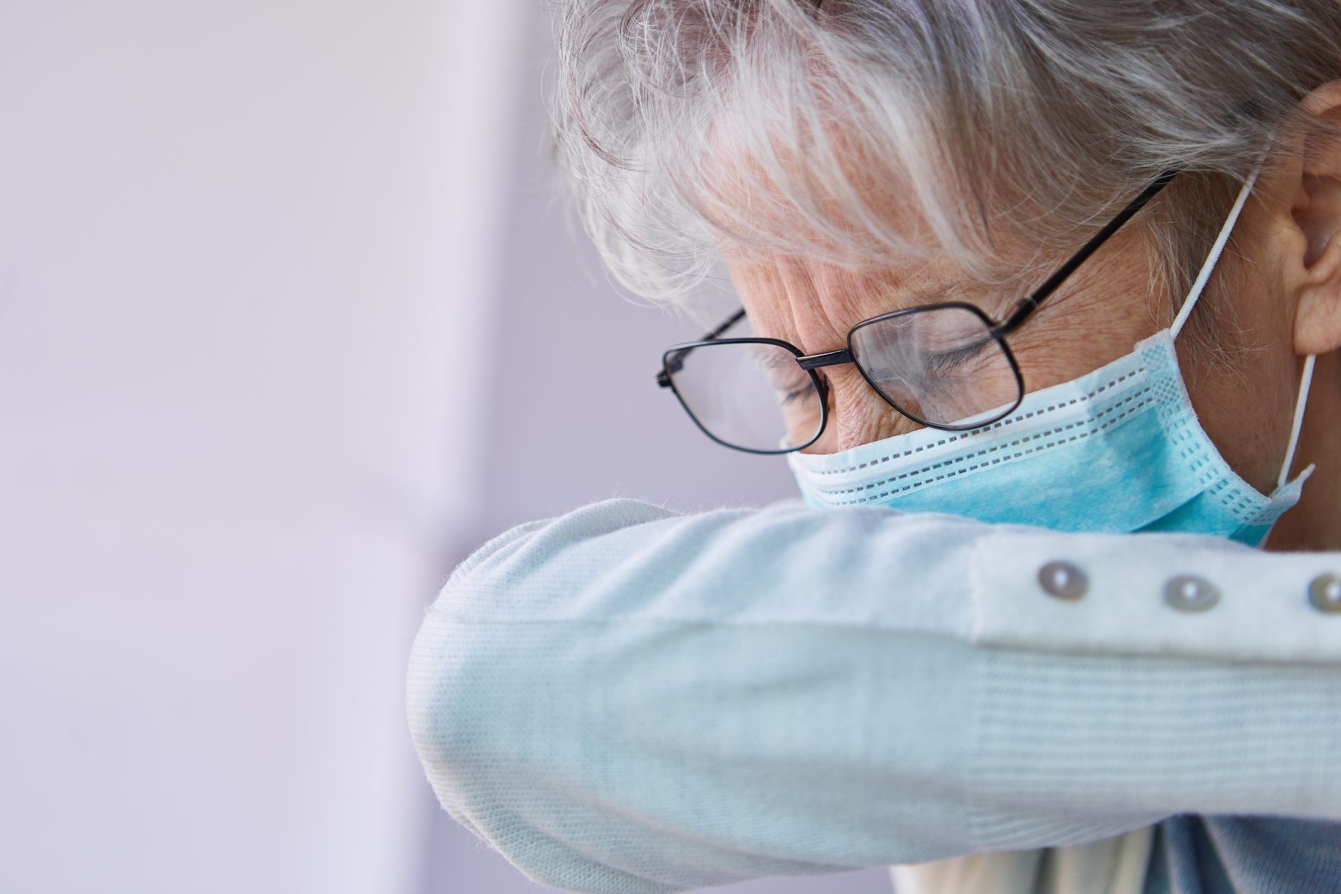 Person in glasses and a blue mask resting their head on a light blue sleeve