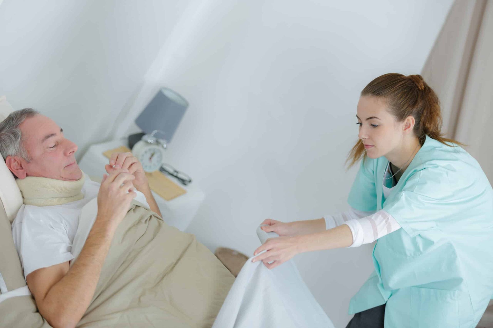 Nurse adjusting blanket of patient in bed with neck brace.