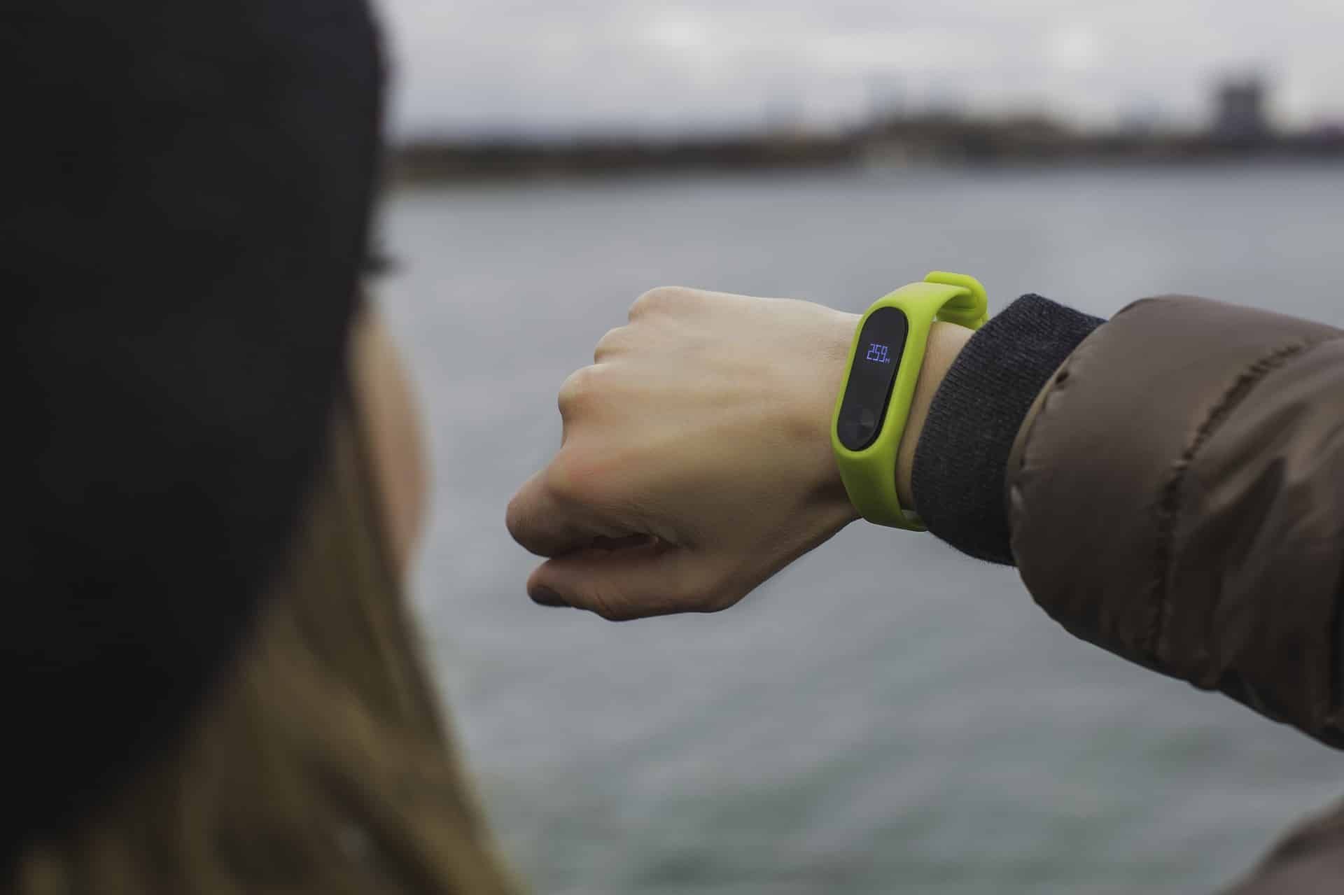 Person wearing a green fitness tracker outdoors near water; checking the device.