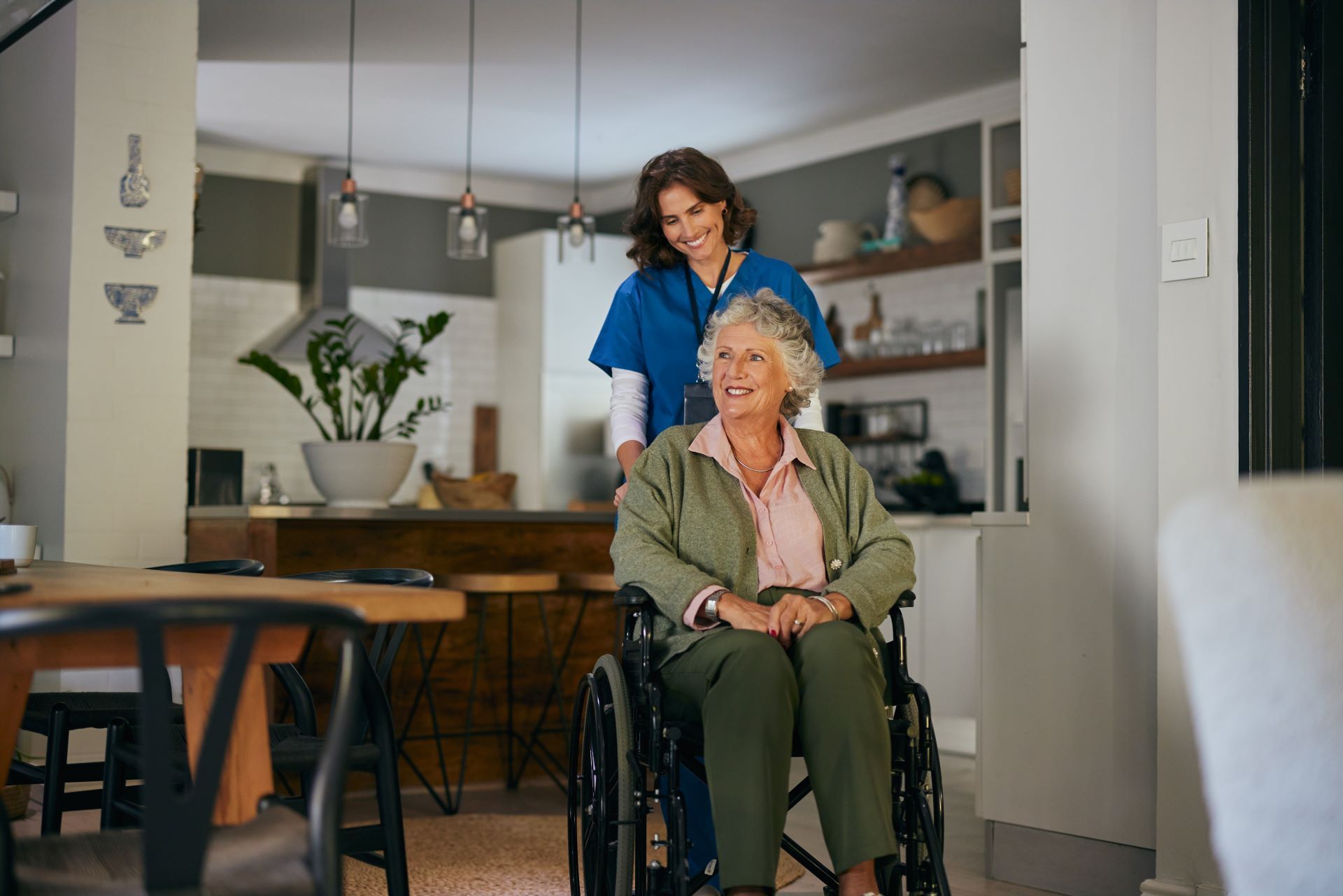 Caregiver standing behind woman in wheelchair in a bright home kitchen