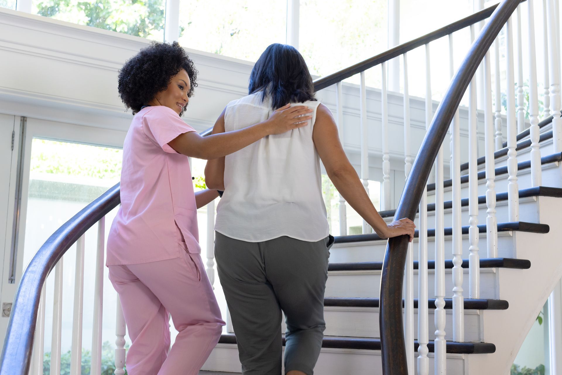 Two women walking up a staircase, one supporting the other by the back.