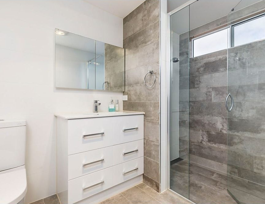 Modern Bathroom with White Vanity, Mirror, Toilet, and Gray Tiled Glass Shower — Rivbuild In Uranquinty, NSW
