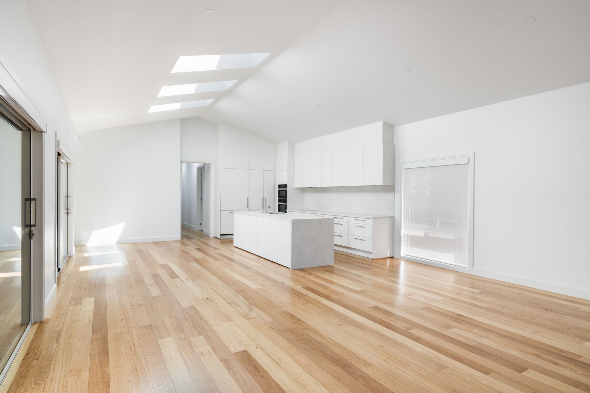 Bright minimalist kitchen with white cabinets, island, and hardwood floors in an open living space