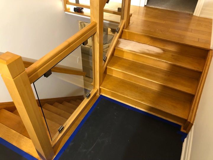 A refinished wooden staircase with a glass railing in a house