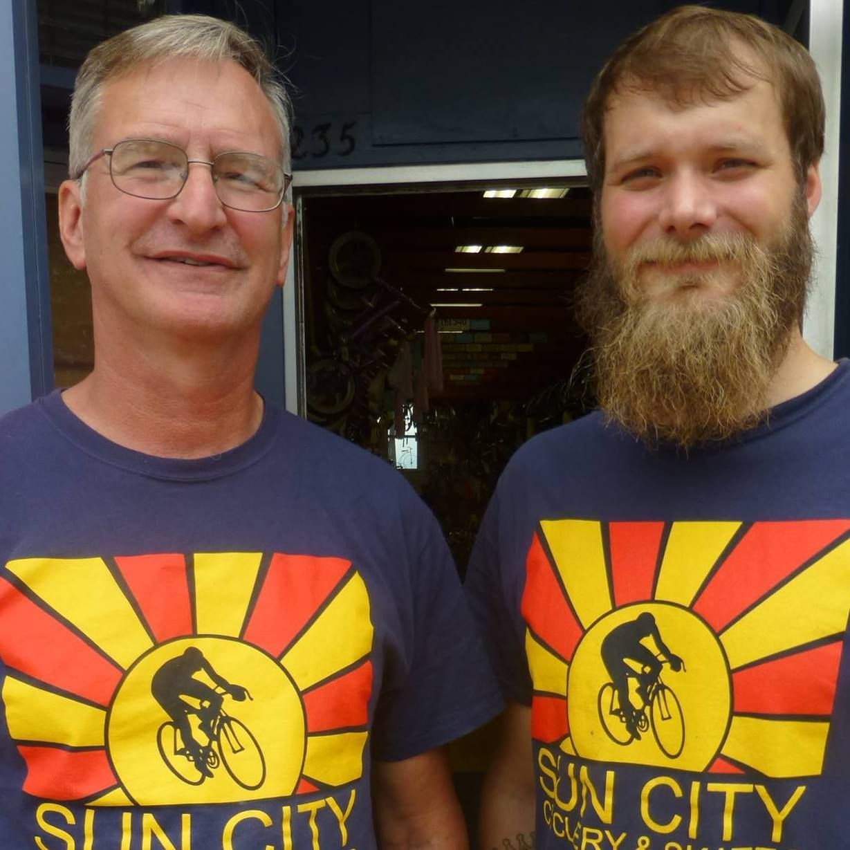 Two smiling men in Sun City T-shirts standing side by side outdoors