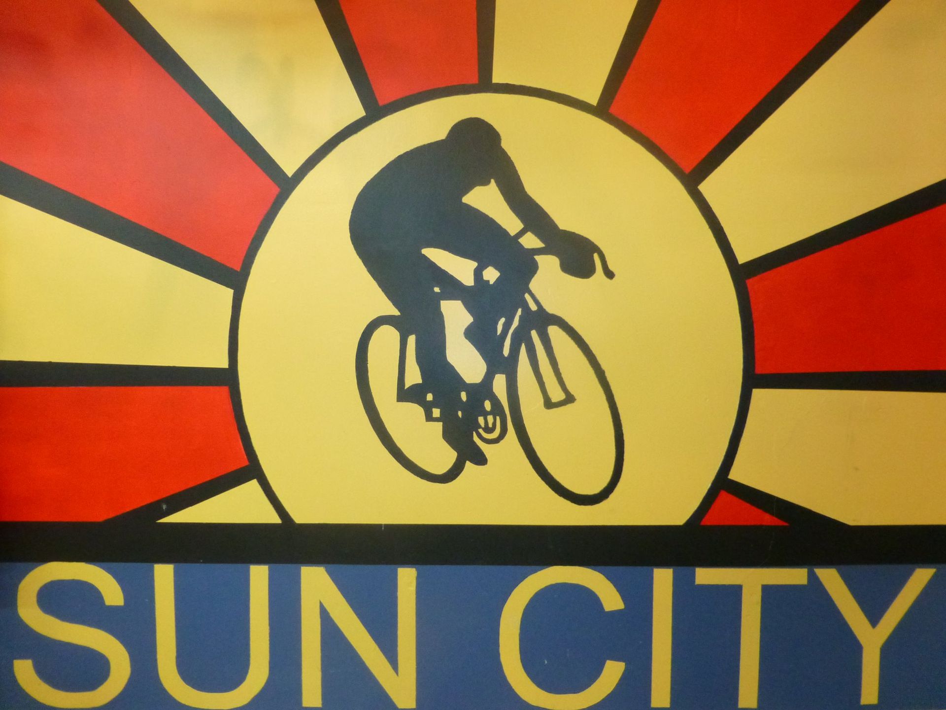 Sun City sign with a cyclist silhouette over a yellow sun on a red and orange background