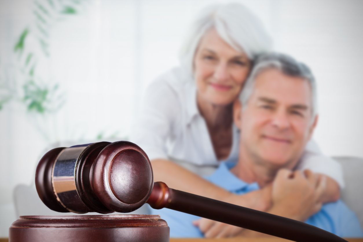 Gavel in foreground; older couple embracing in background, smiling.