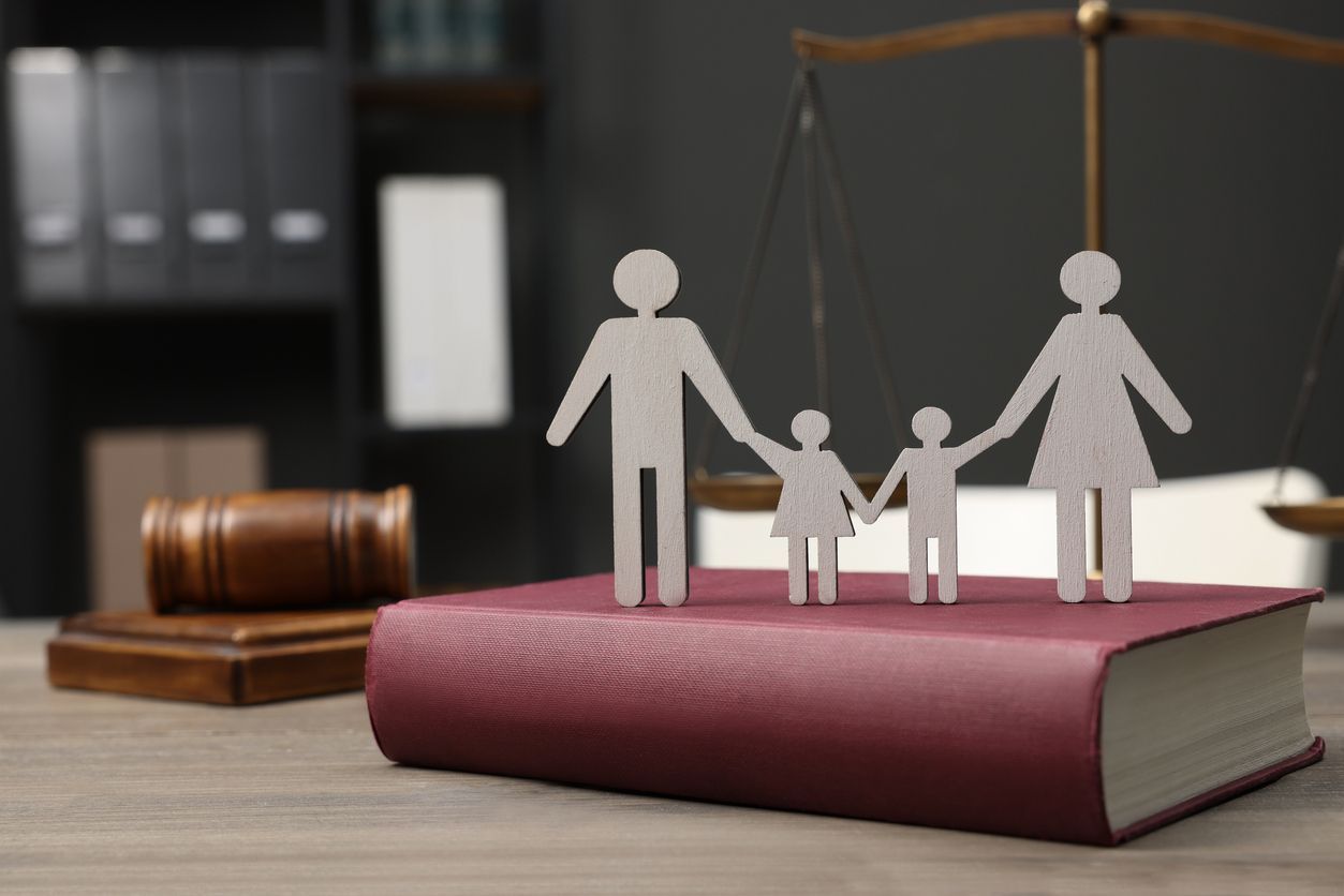 Paper family figures atop a law book, scales of justice and gavel in background.
