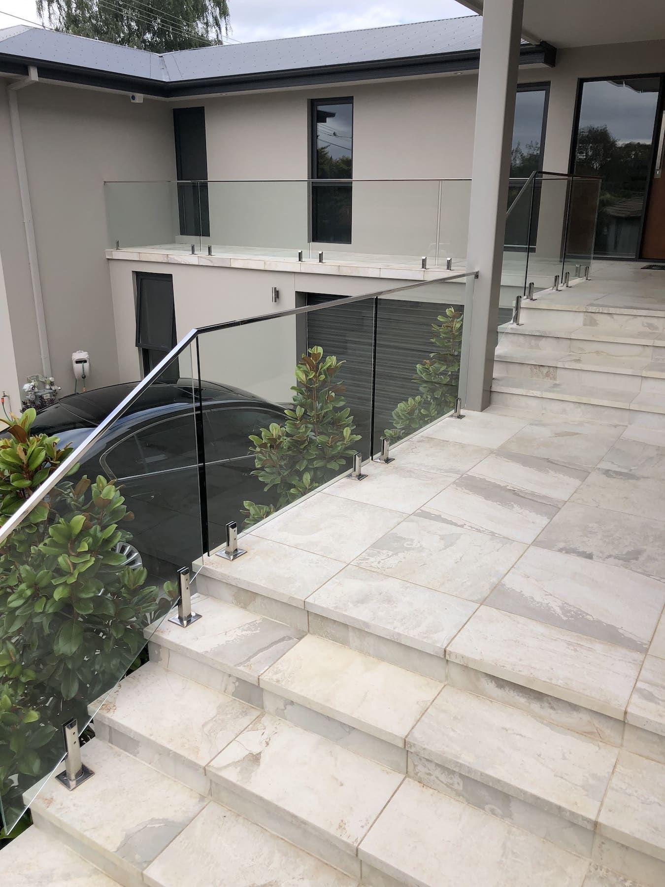 Glass railings on stone steps leading up to a two-story house with dark windows.