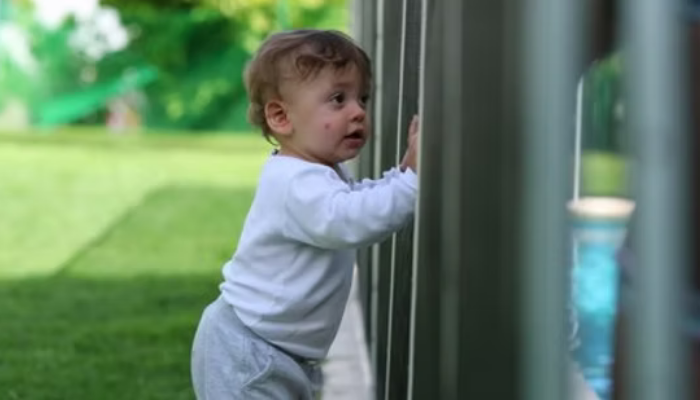 Toddler standing next to a pool fence, highlighting the importance of compliant and safe fencing to protect children.