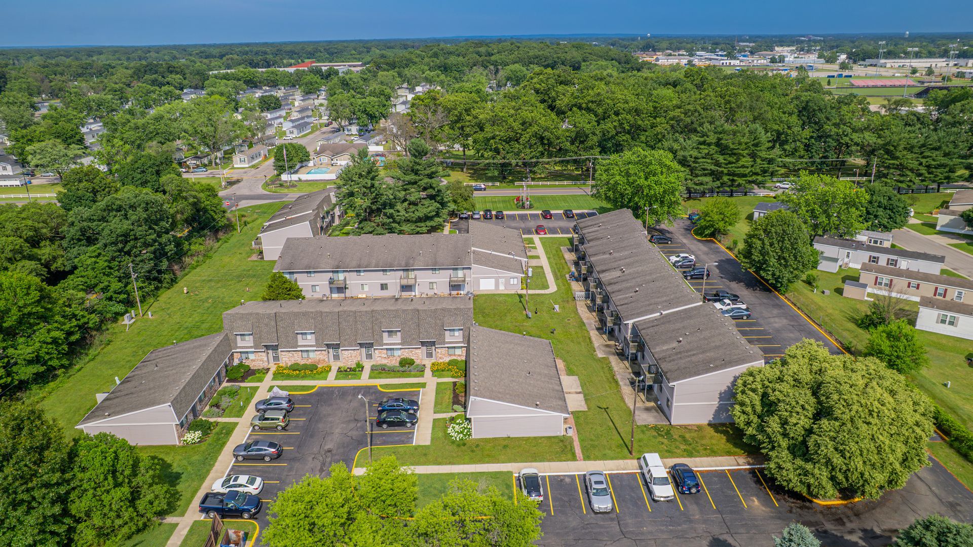 Aerial view of apartment complex with parked cars, surrounded by trees and green lawns.