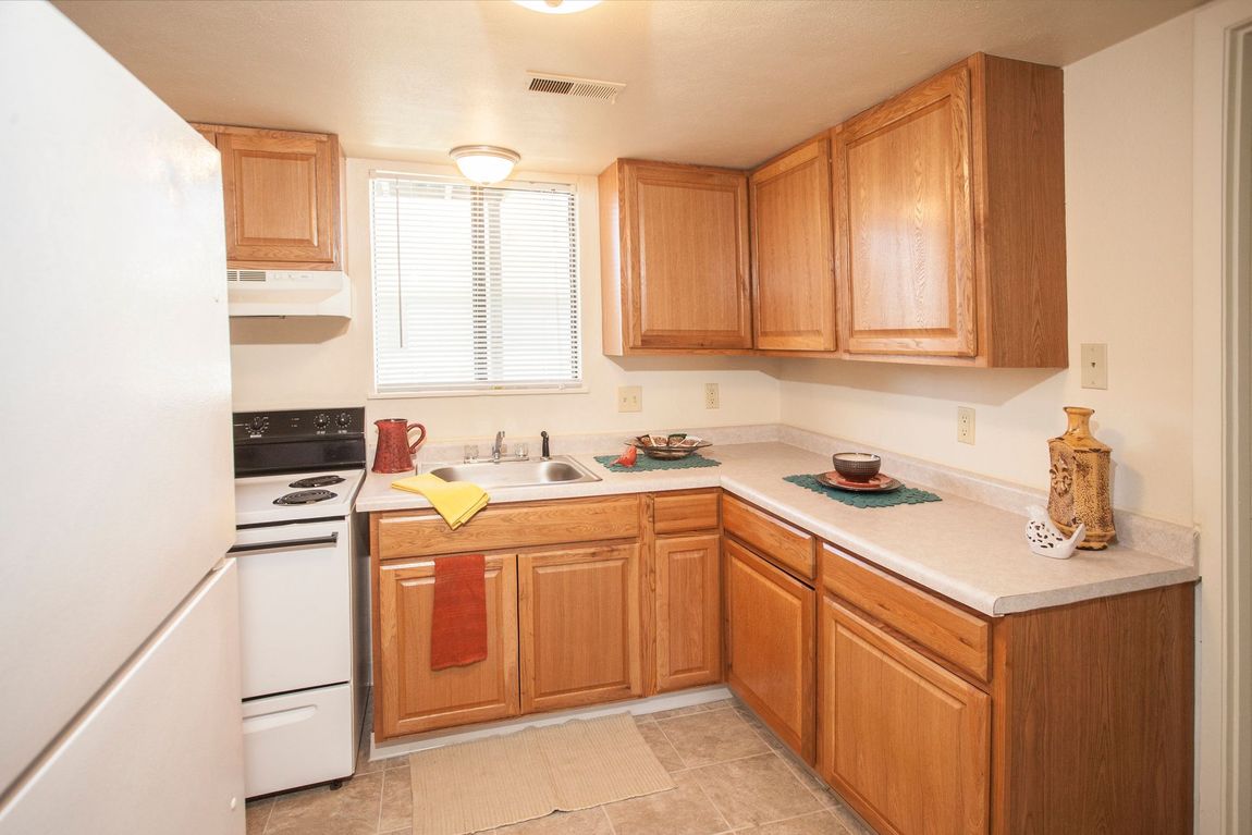 Small kitchen with wooden cabinets, white appliances, and a window above the sink.
