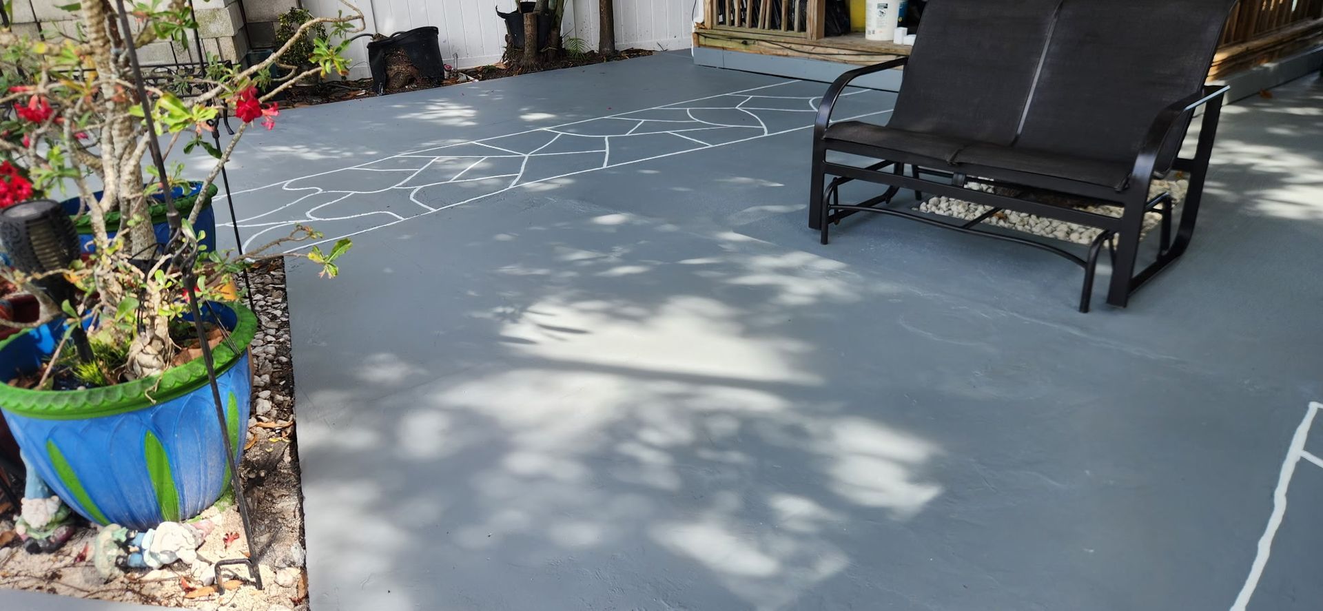 Patio with gray concrete floor, potted plants, and a black lounge chair in sunlight.