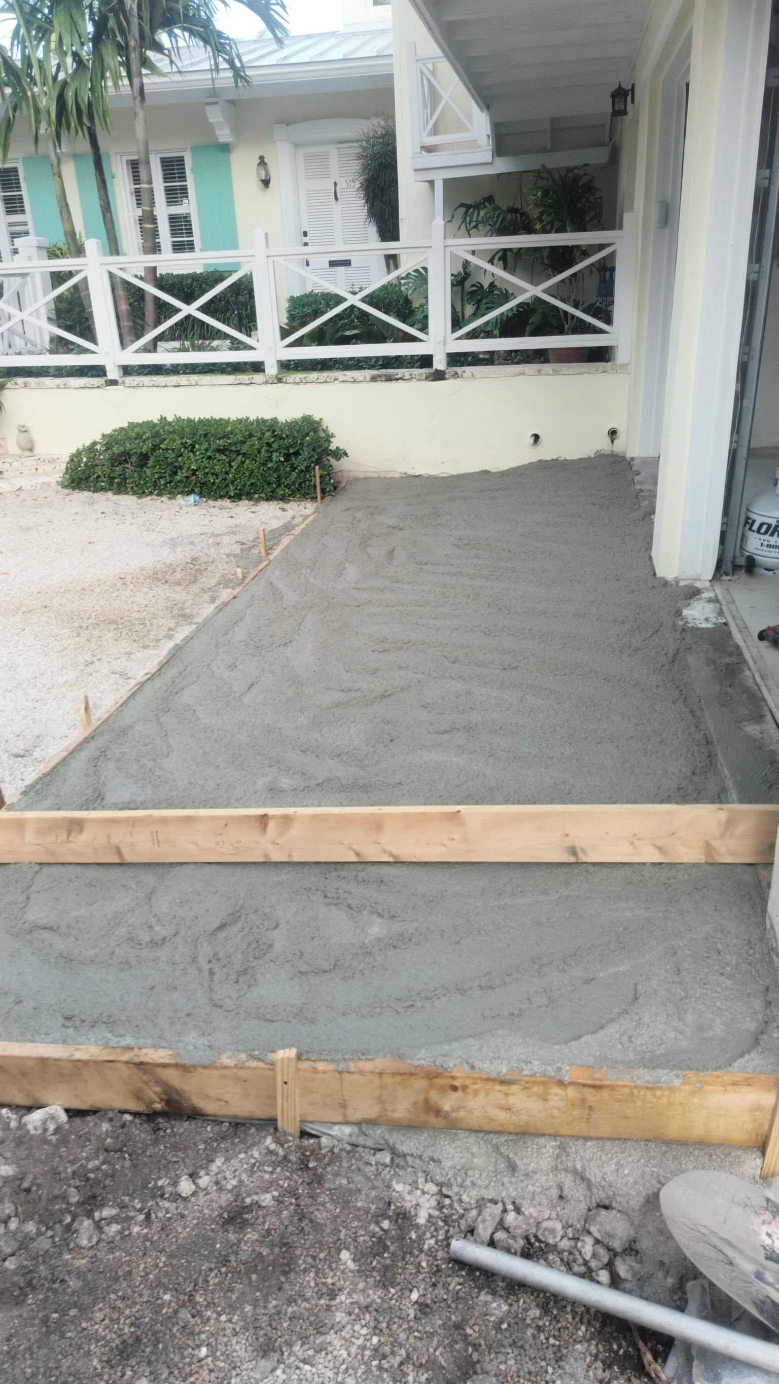 Concrete ramp with wooden edging leading to a porch with white railing and turquoise house siding.