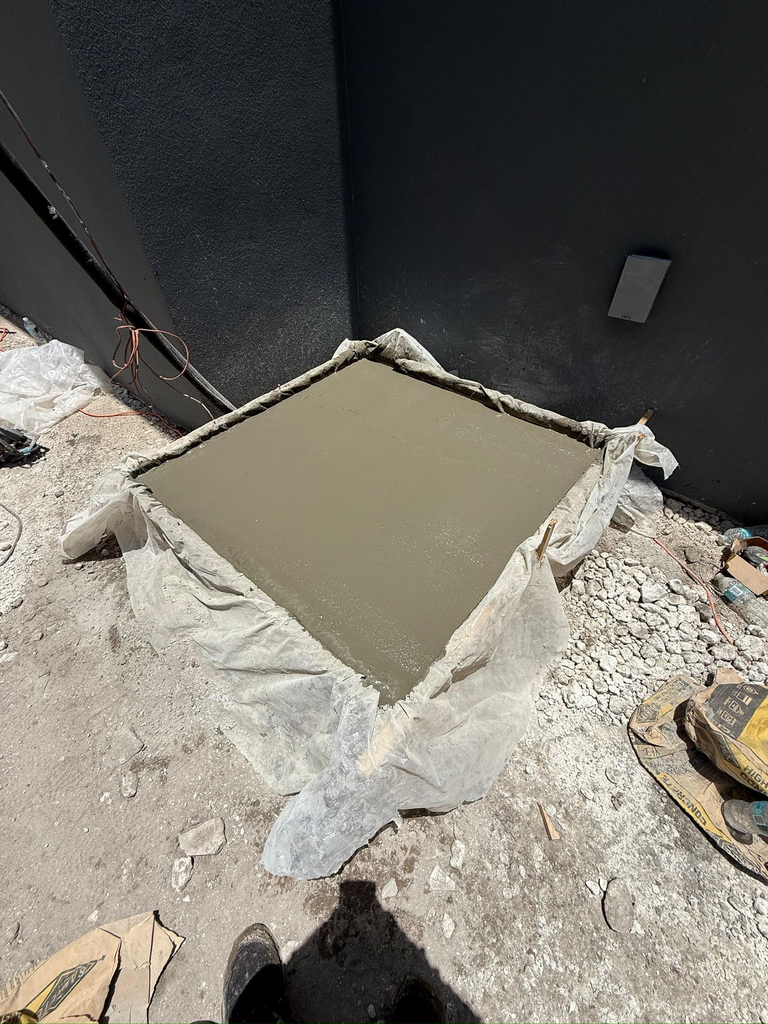 Fresh concrete patch in a roof corner beside gravel and dark walls