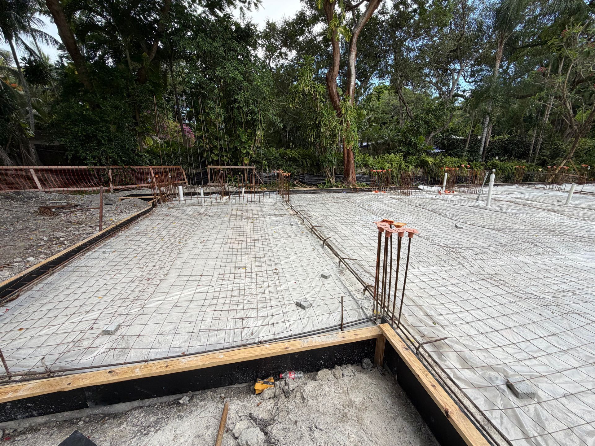 Concrete slab foundation under construction with exposed rebar and wooden formwork outdoors