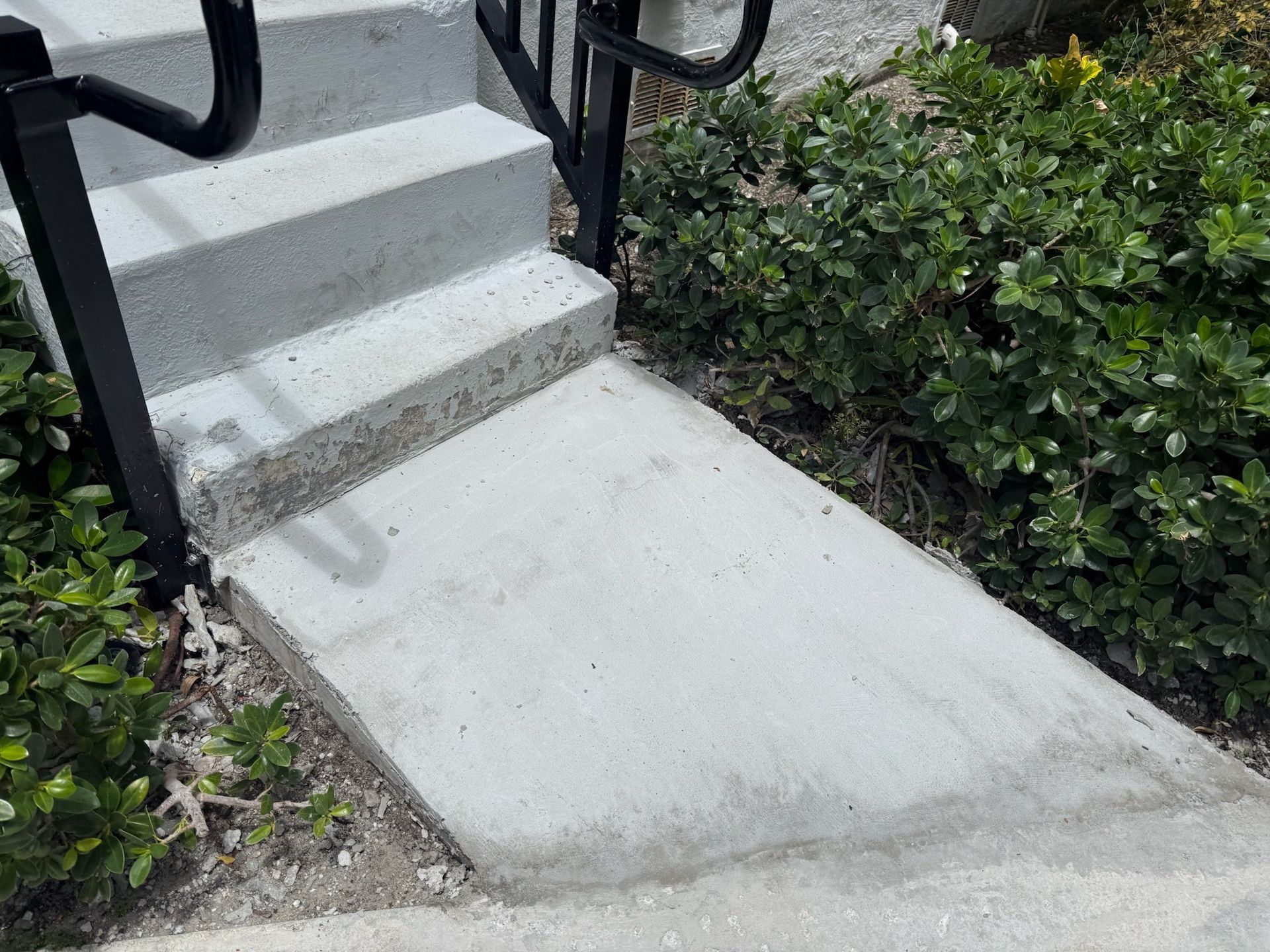 Concrete ramp beside outdoor stairs and hedges leading to a walkway