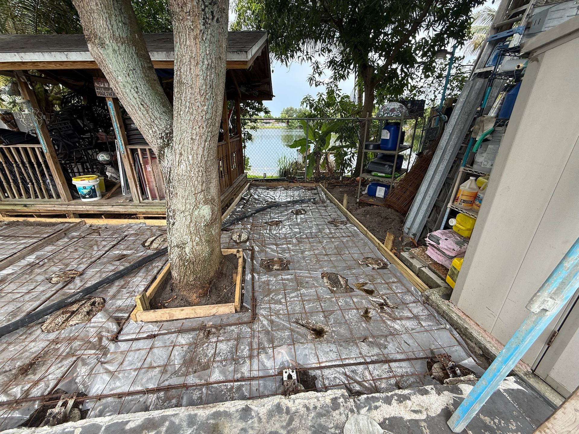 Stone patio with a large tree, wooden deck, and a small shed beside a garden path.