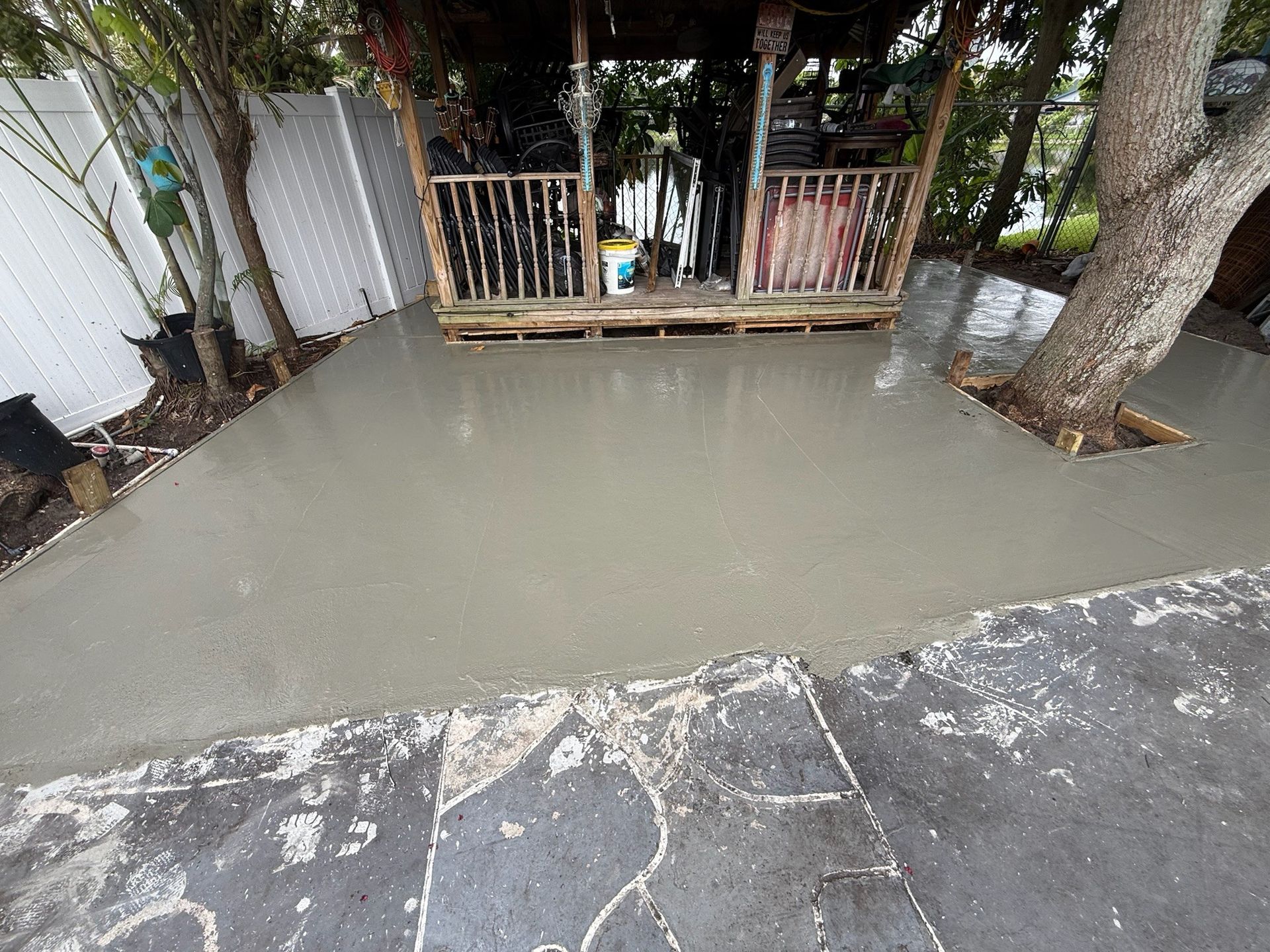 Flooded driveway with muddy water pooled beside a wooden gate and a large tree.