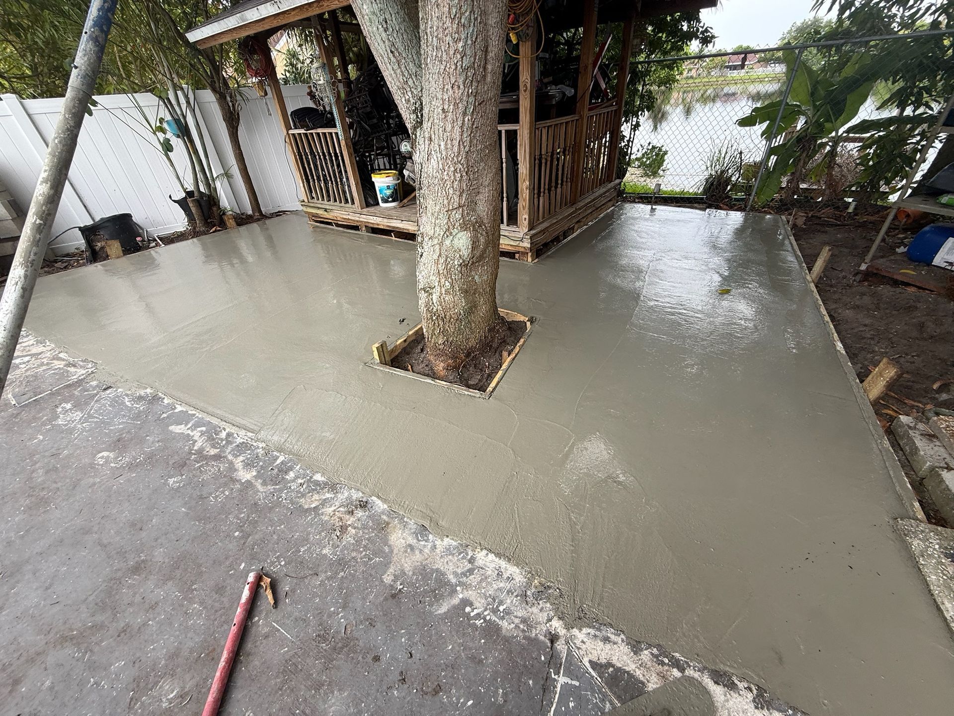 Fresh concrete patio with a tree cutout, surrounded by a wooden structure and water nearby