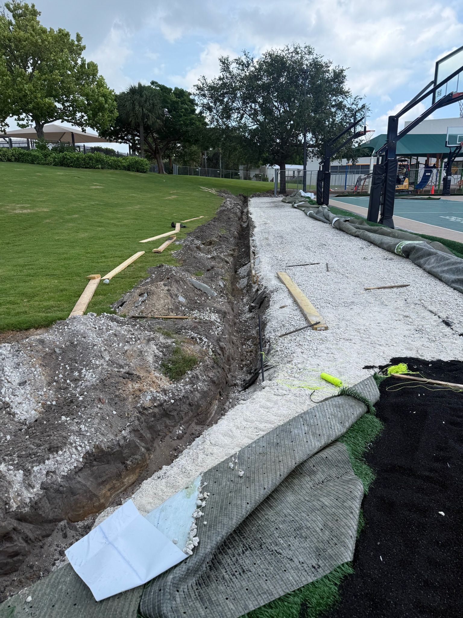 Damaged gravel path beside a grassy slope, with a broken concrete edge and construction barriers.