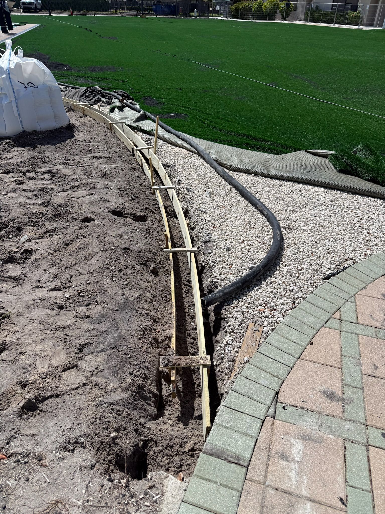 Exposed cables and a black hose along a gravel path beside green artificial turf