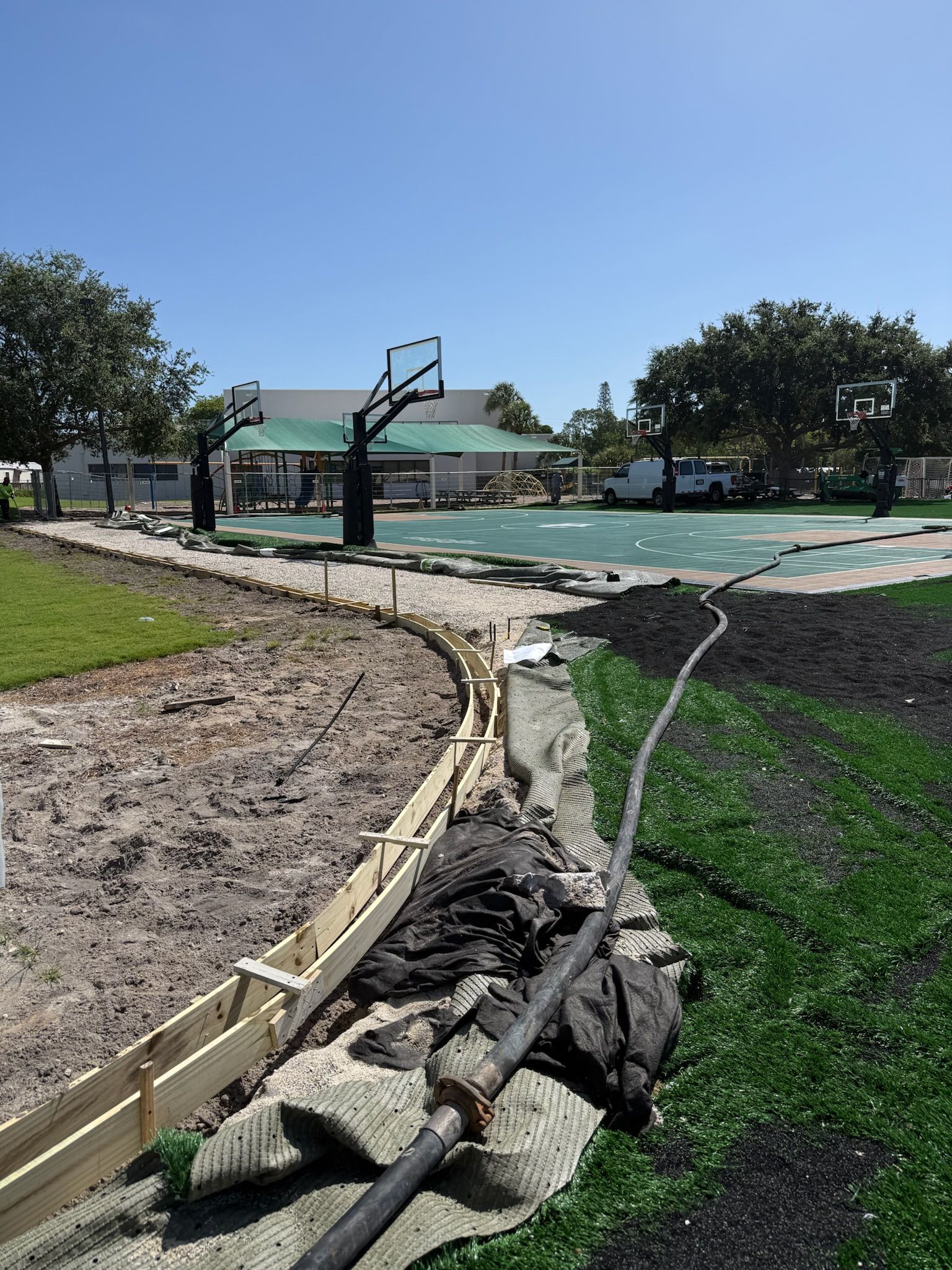 Damaged basketball court with cracked pavement, rubble, and a bent hoop under a clear sky