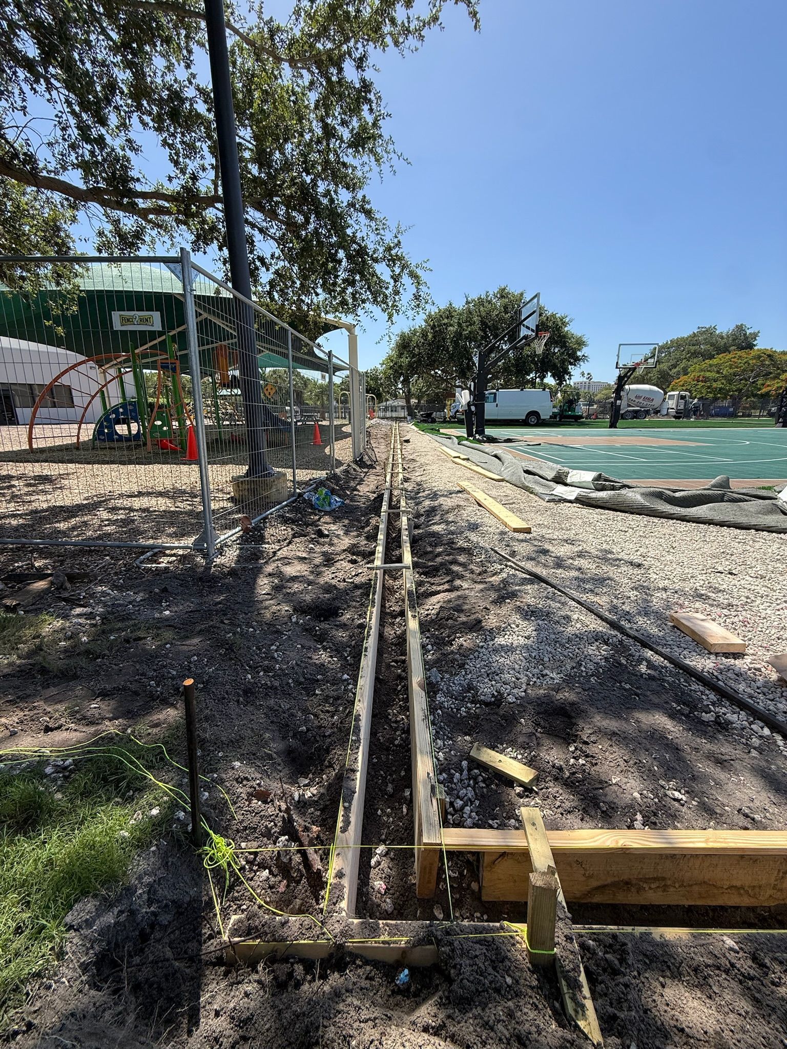 Railway track under construction beside a beach, with gravel, trees, and turquoise water.