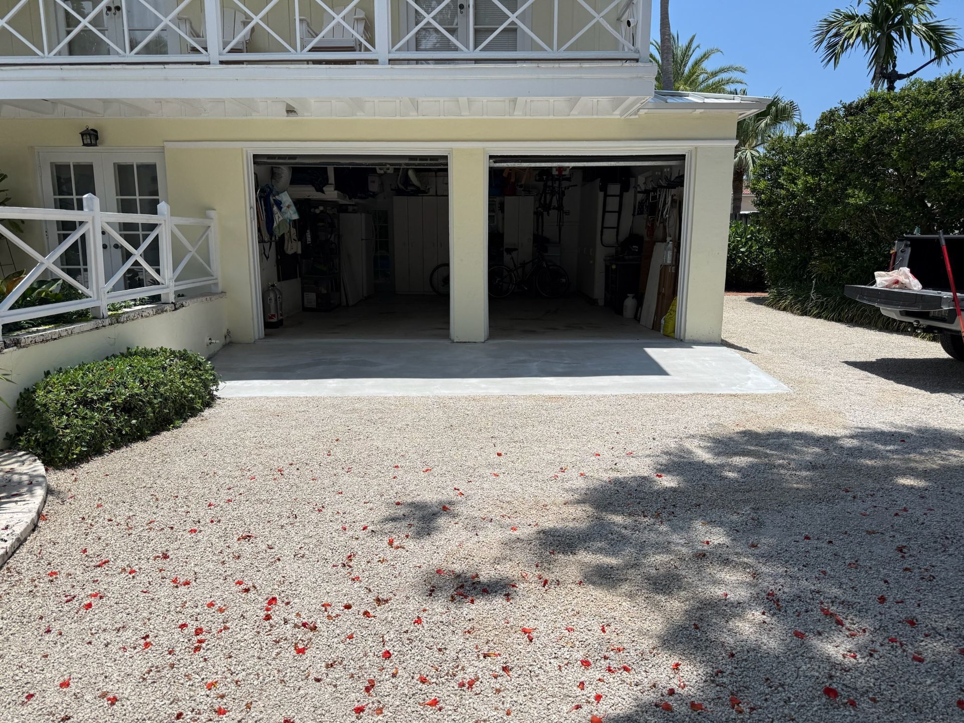 Two-car garage entrance beside a white house, with a gravel driveway and sunlit shadows.