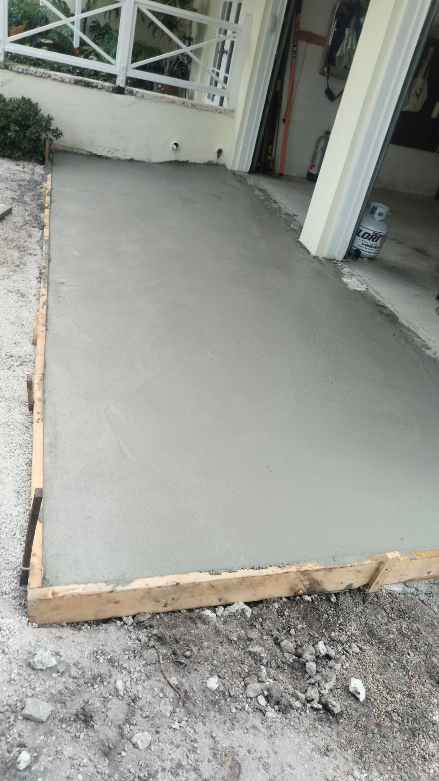 Freshly poured concrete slab at a building entrance with rough gravel around it.