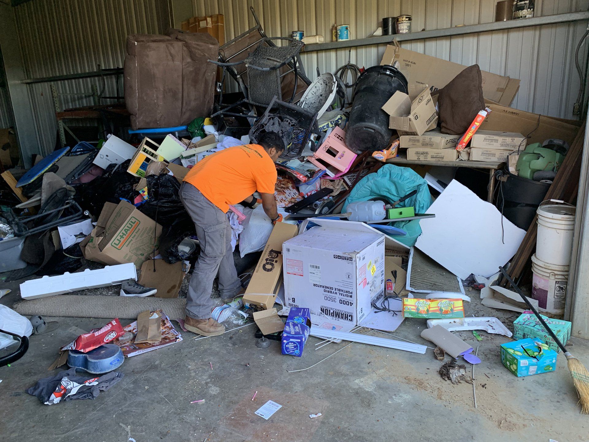 Person sorting through a pile of discarded items inside a cluttered garage.