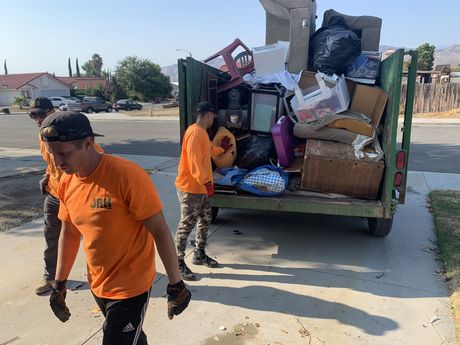 Workers loading trash into a green garbage truck in a suburban driveway.