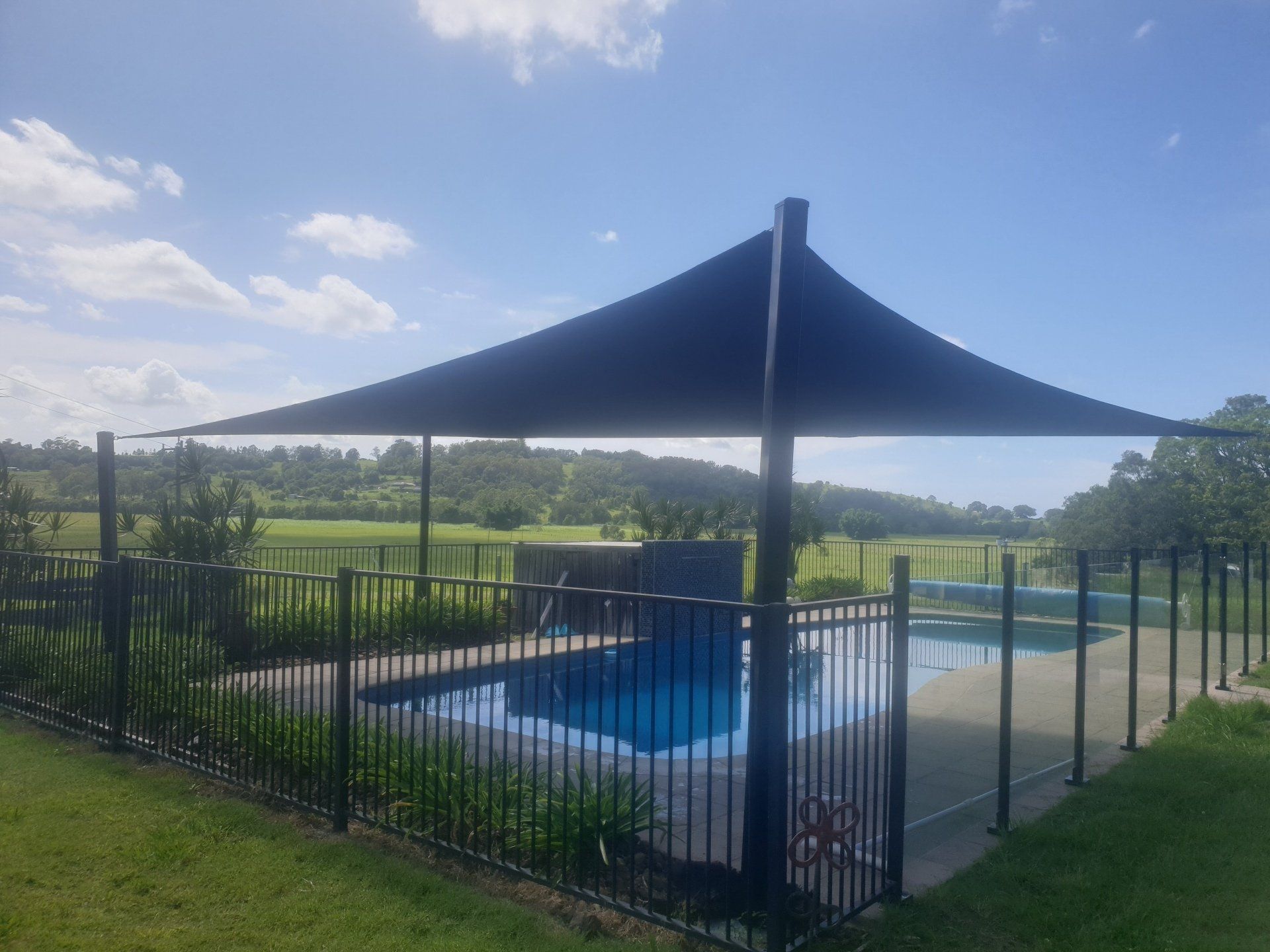 A large umbrella is covering a swimming pool behind a fence-Smart Shades Lismore NSW