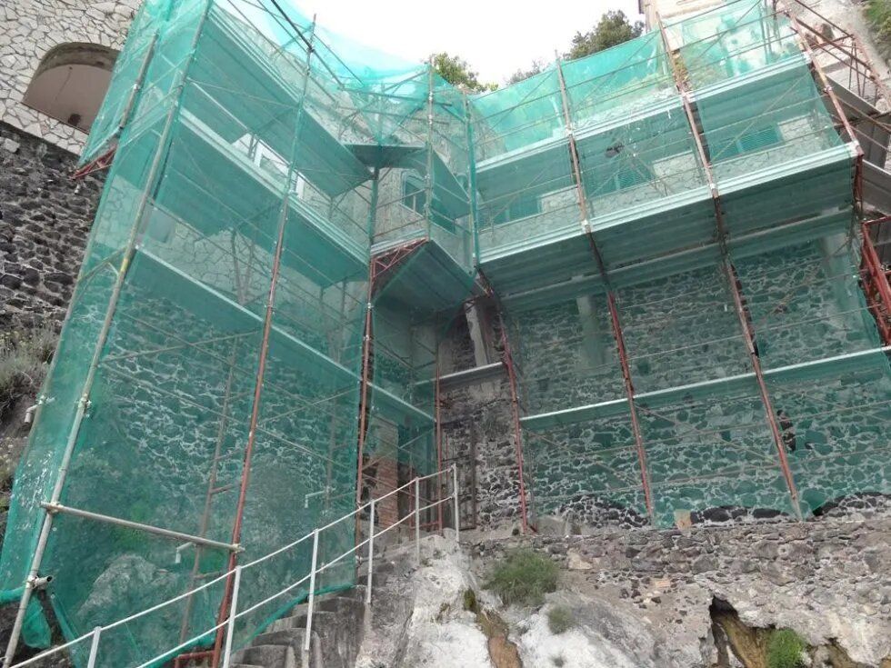 Rete di protezione verde che copre un edificio in pietra in fase di ristrutturazione, con impalcature