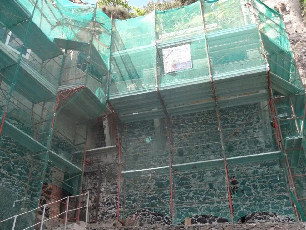 Edificio in fase di ristrutturazione, impalcato e avvolto da una rete di sicurezza verde.