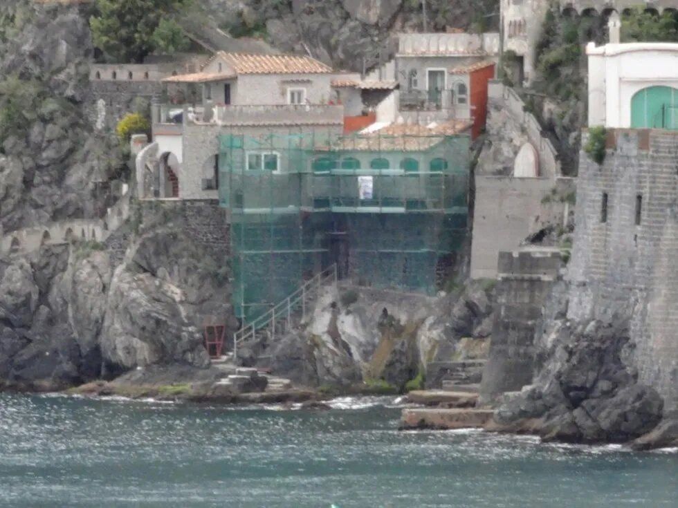 Edifici a picco sul mare, con una torre in pietra e un edificio ricoperto da impalcature verdi.
