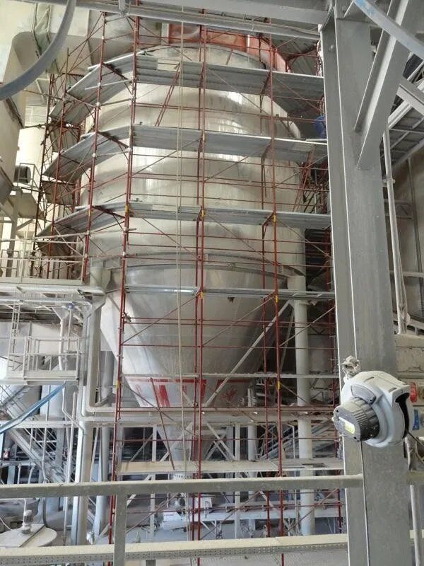 Grande silo industriale in costruzione, circondato da impalcature metalliche e supporti strutturali