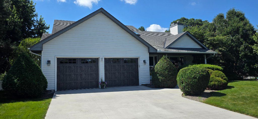 Suburban house with a double garage, white facade, and a driveway bordered by green lawn and shrubs